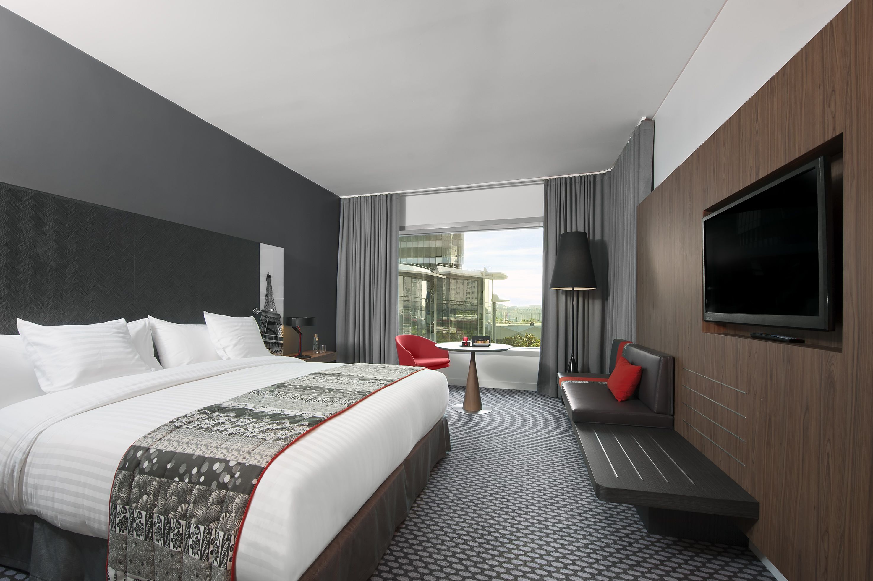 Une chambre d’hôtel moderne dotée d’un grand lit, d’un coin salon, d’une télévision et offrant une vue sur la ville.