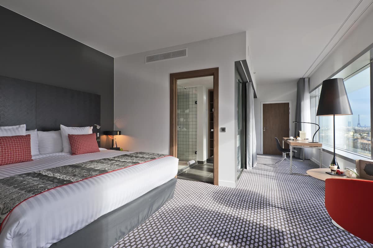 A modern hotel room with a large bed, a desk, and a view of the city.