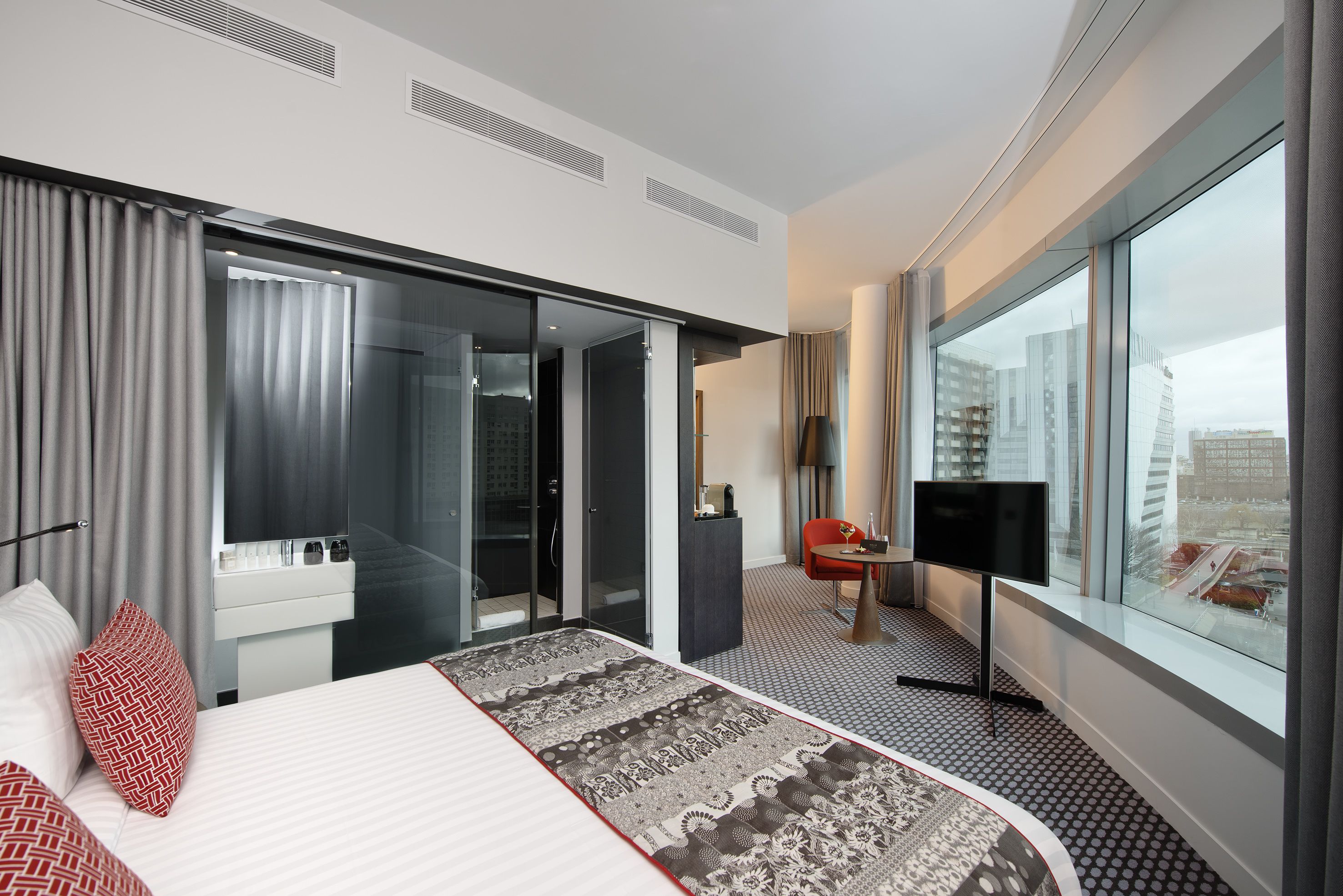A modern hotel room with a large bed, a TV, a desk, and a view of the city.