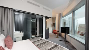 A modern hotel room with a large bed, a TV, a desk, and a view of the city.