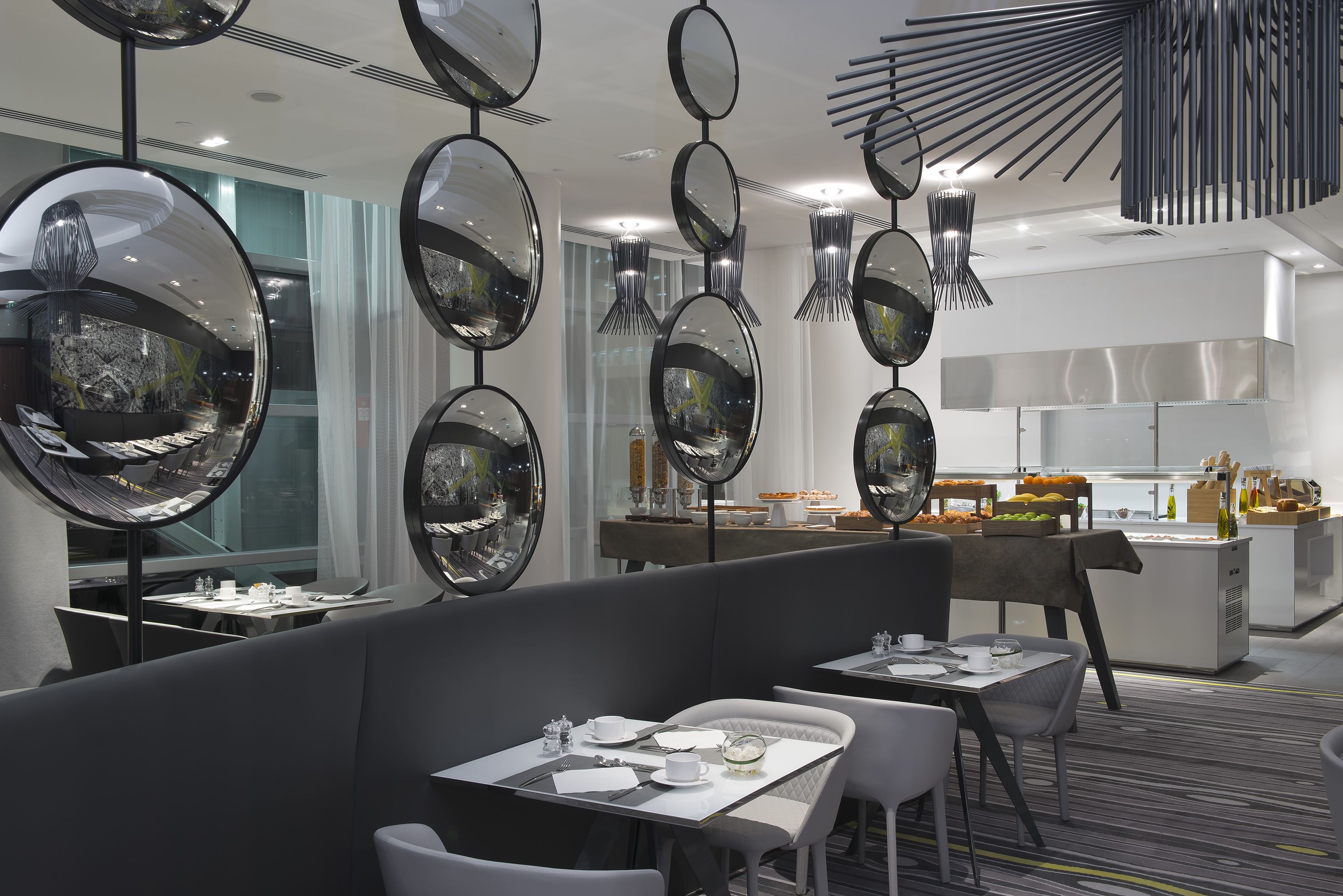 Un restaurante moderno con espejos redondos en el techo, mesas blancas y una zona de bufé al fondo.