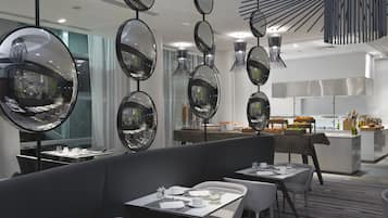 Un restaurante moderno con espejos redondos en el techo, mesas blancas y una zona de bufé al fondo.