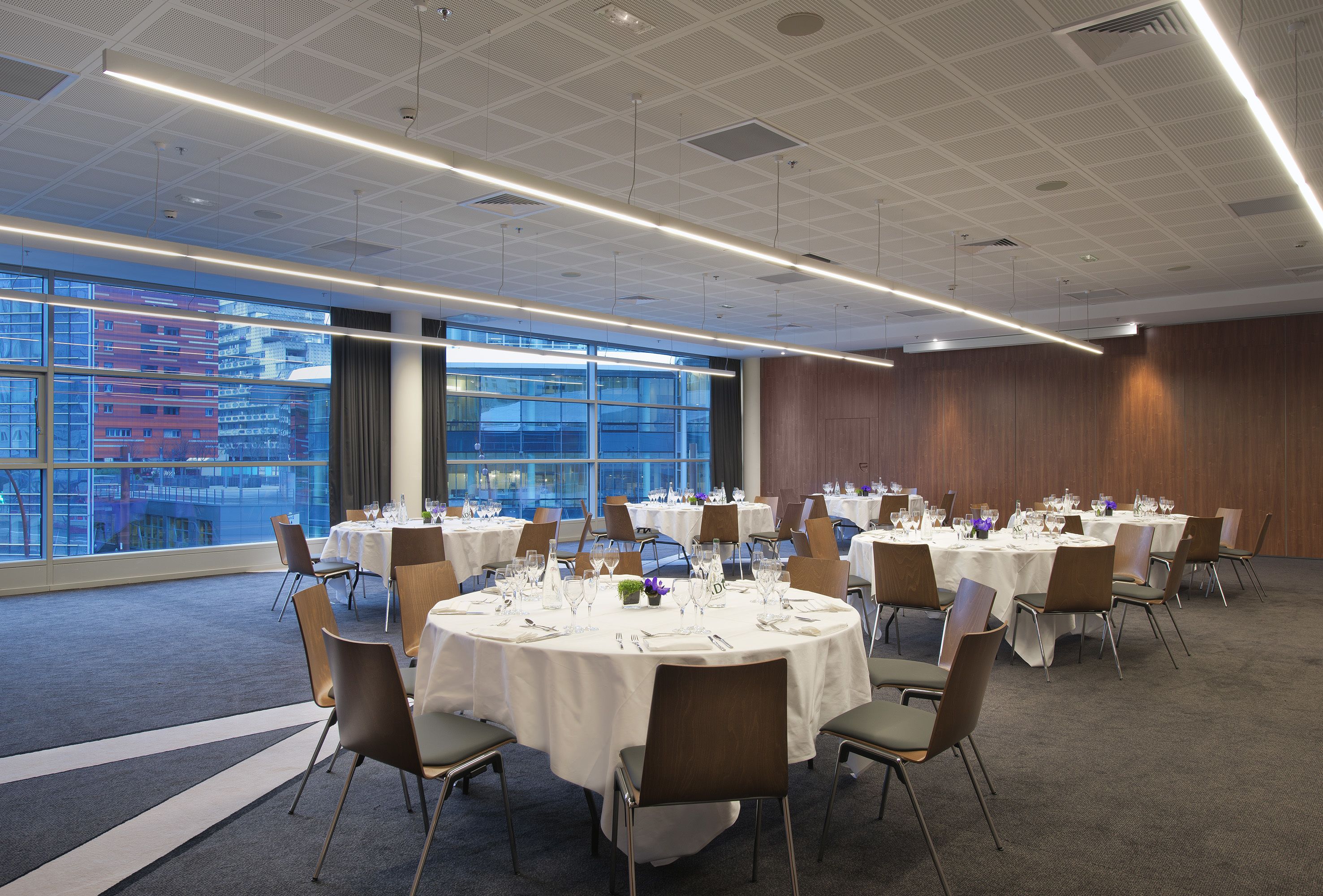 A conference room with round tables, chairs, and a city view through large windows.