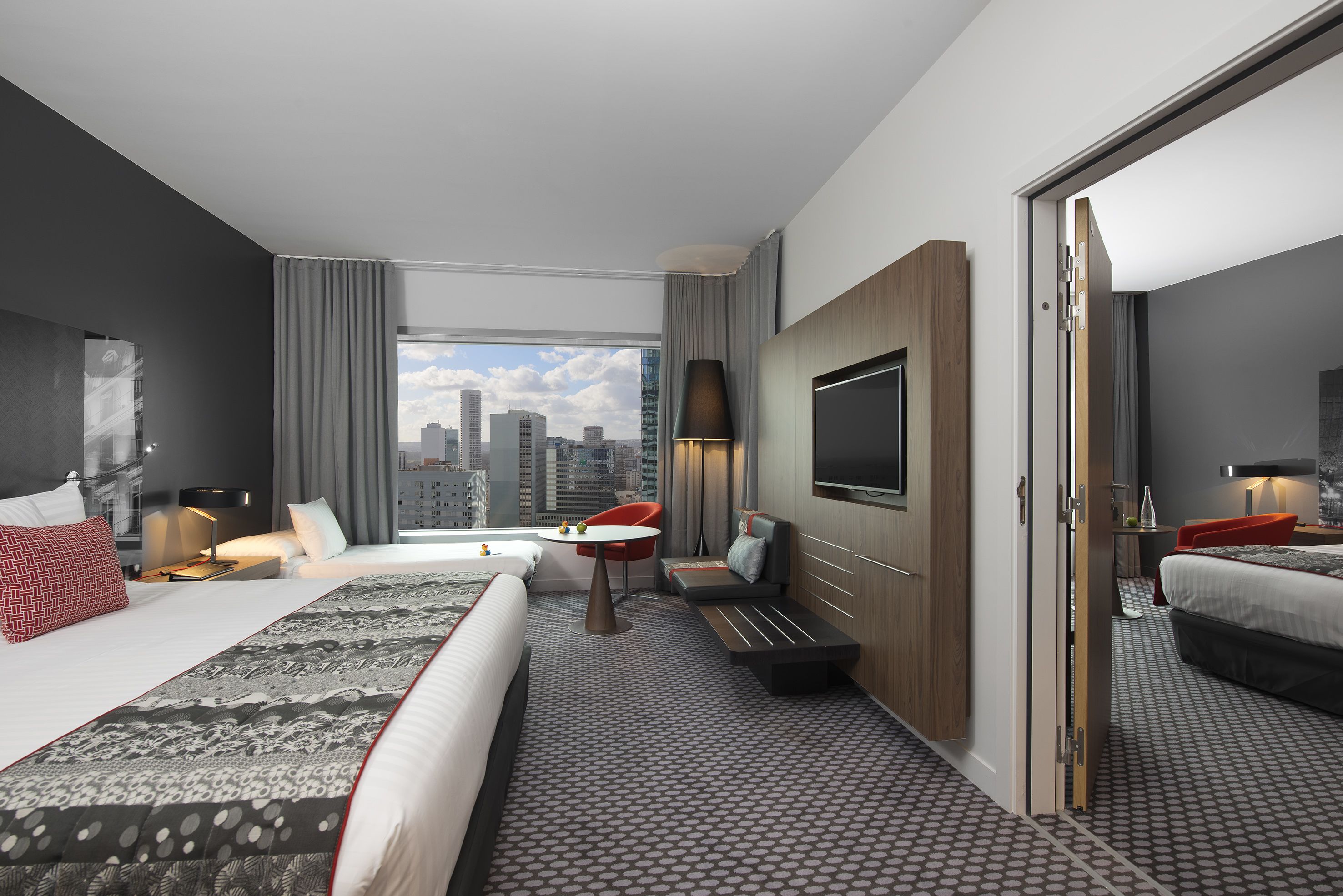 A modern hotel room with a large bed, a desk, a TV, and a city view.