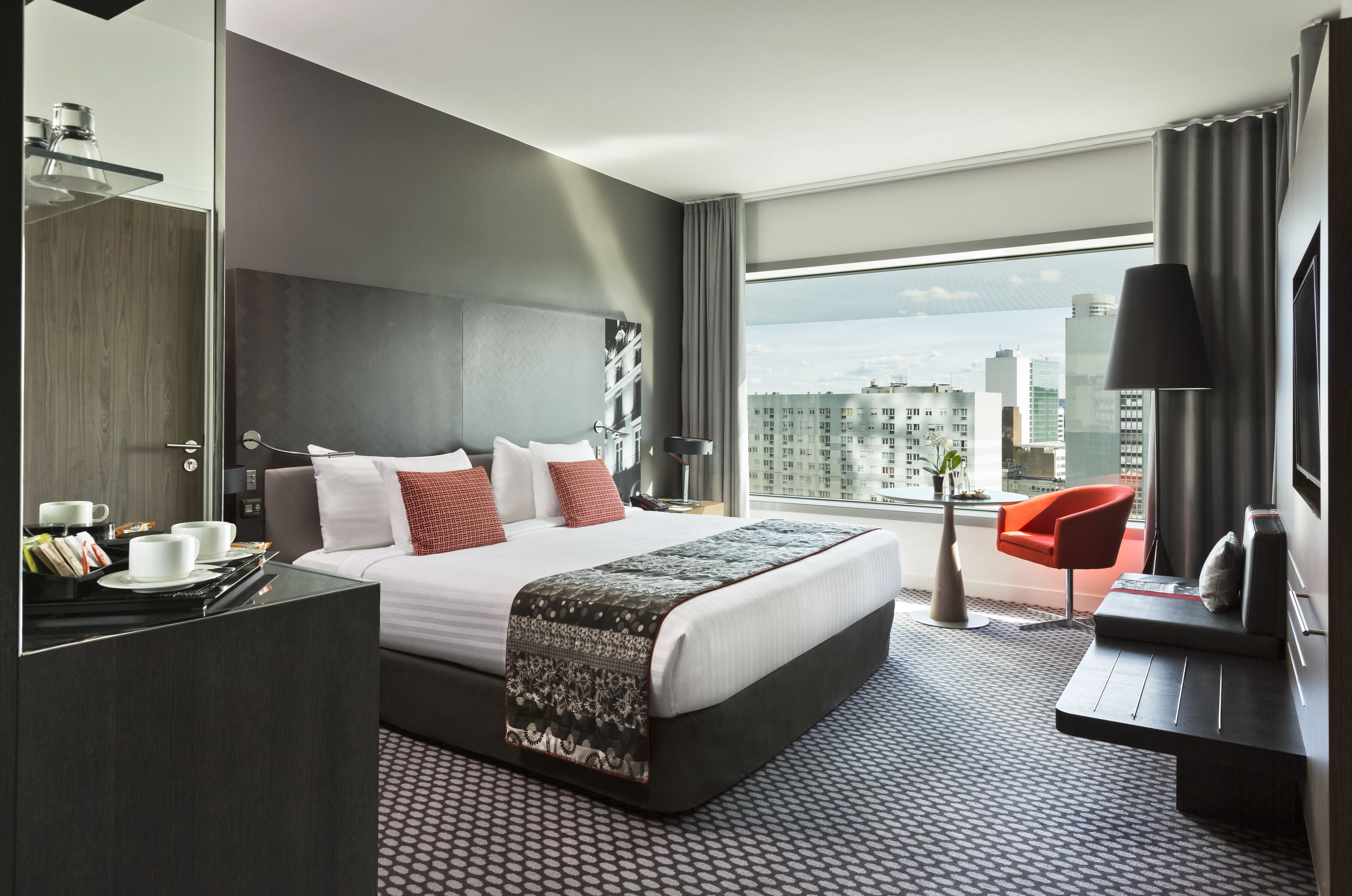 A modern hotel room with a large bed, a desk, a chair, and a view of the city.