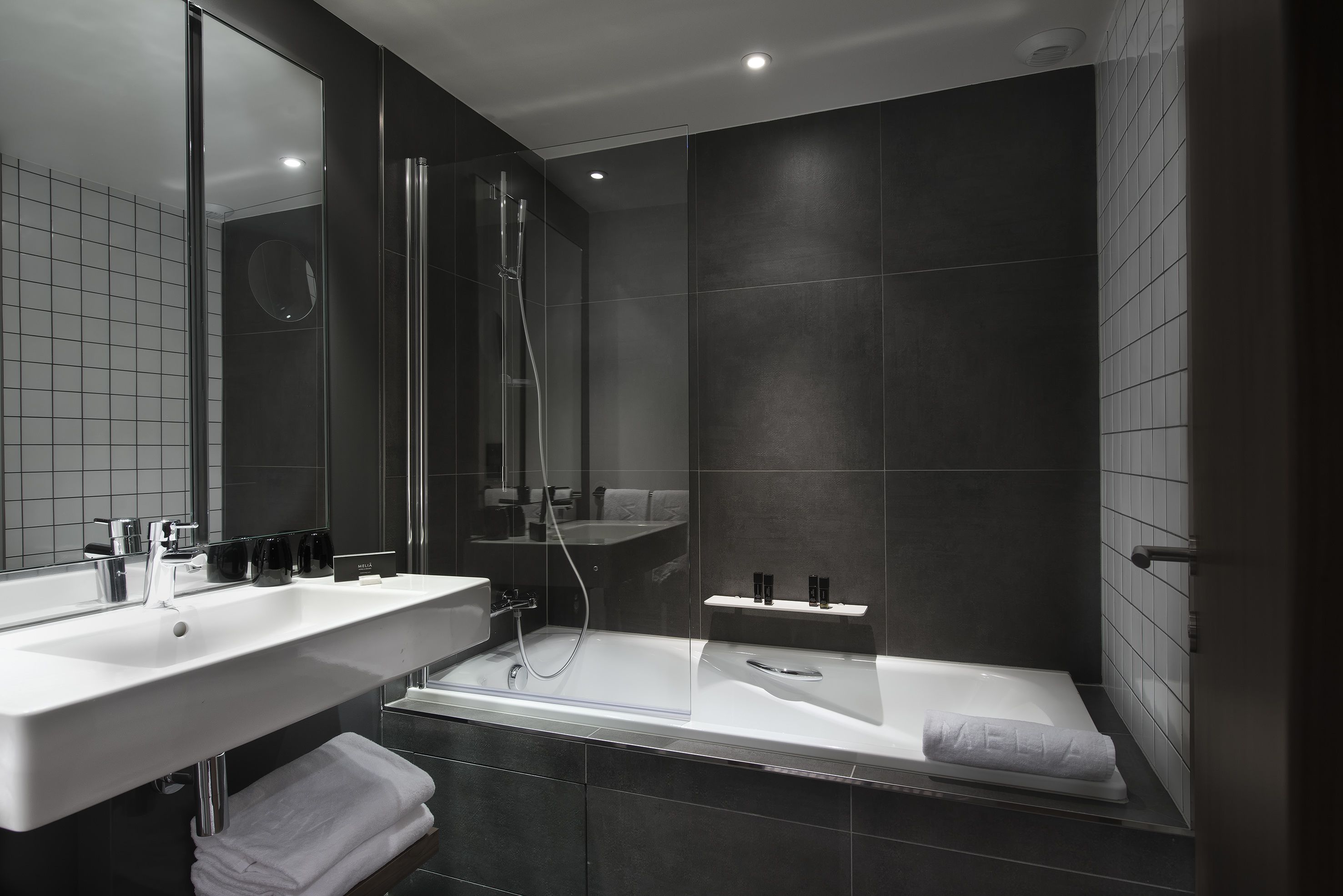 Un baño moderno con dos lavamanos, una bañera y zona de ducha con mampara de vidrio.