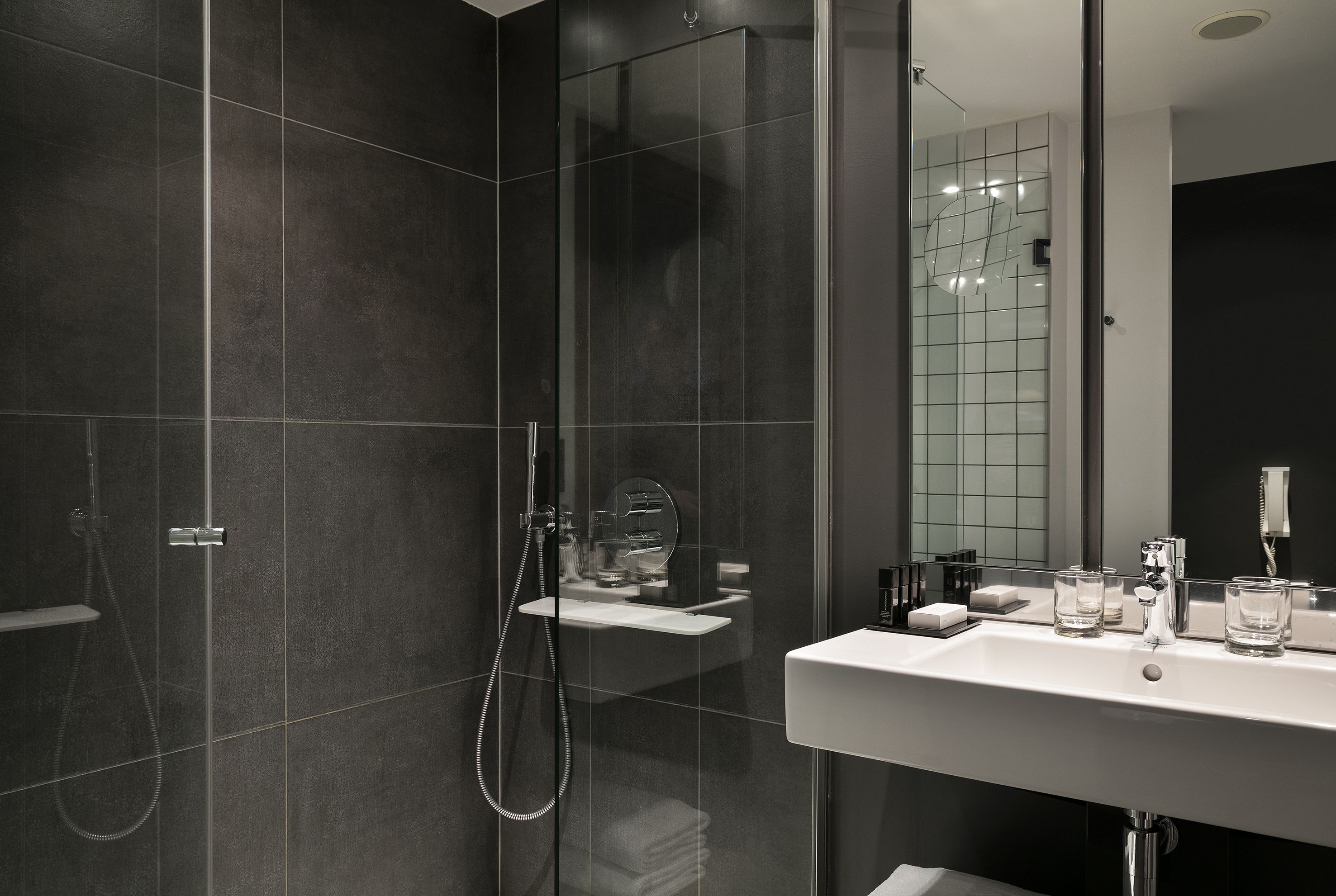 A modern bathroom with a glass-enclosed shower, a white sink, and a mirror reflecting the room.