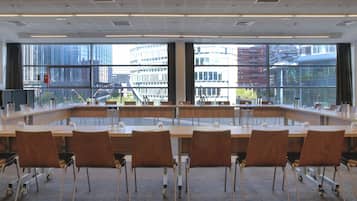 Un salón de conferencias con una larga mesa, sillas y ventanas amplias que dan a una vista de la ciudad.
