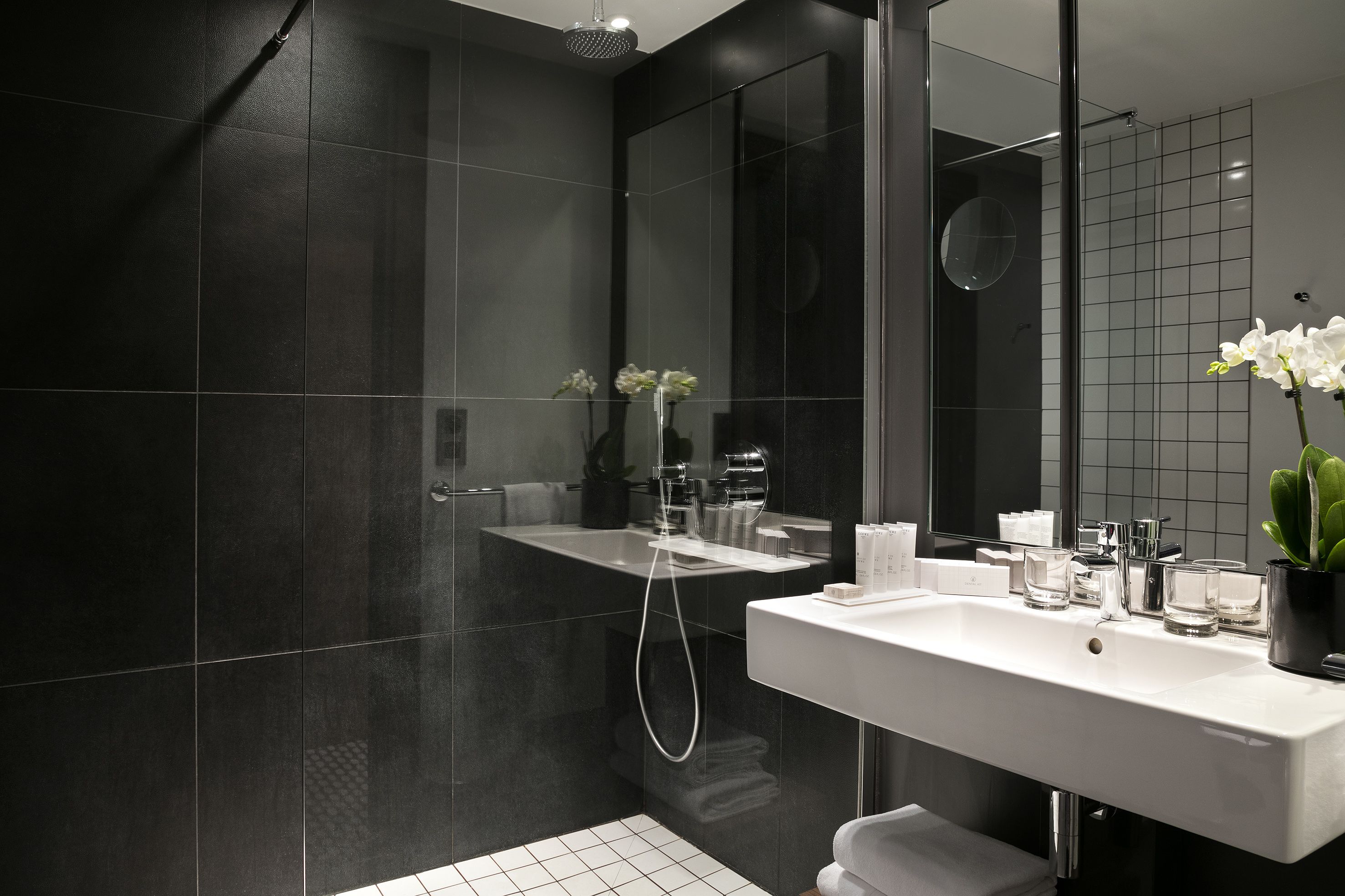 Un baño moderno con azulejos oscuros, un lavabo blanco y una cabina de ducha de vidrio.