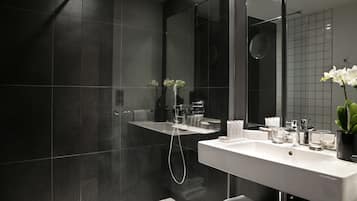 Un baño moderno con azulejos oscuros, un lavabo blanco y una cabina de ducha de vidrio.
