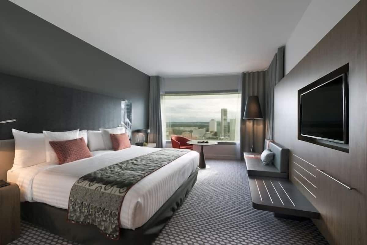 A modern hotel room with a large bed, a seating area, a TV, and a city view.