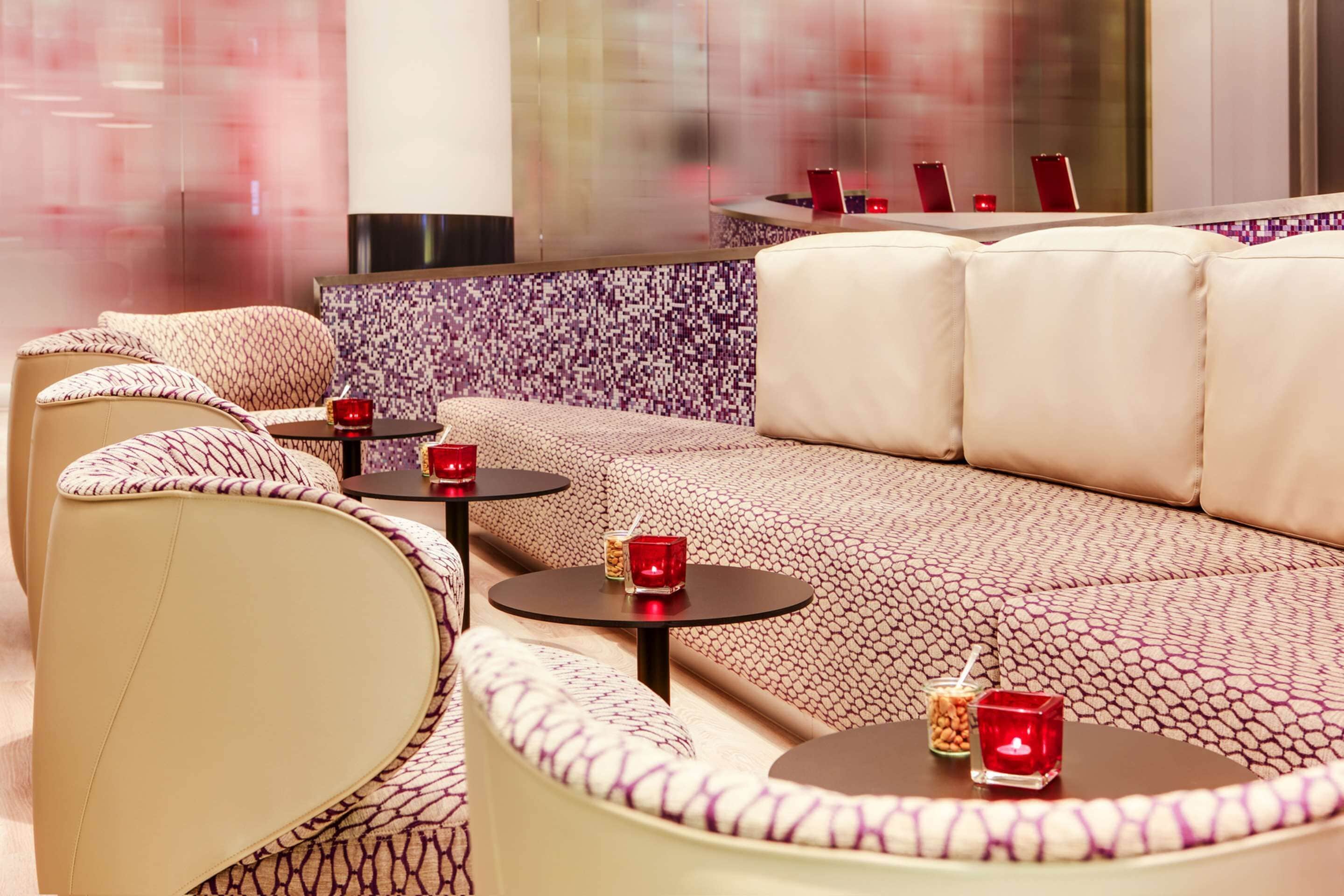 A modern lounge area with a patterned sofa, round tables, and red candles.