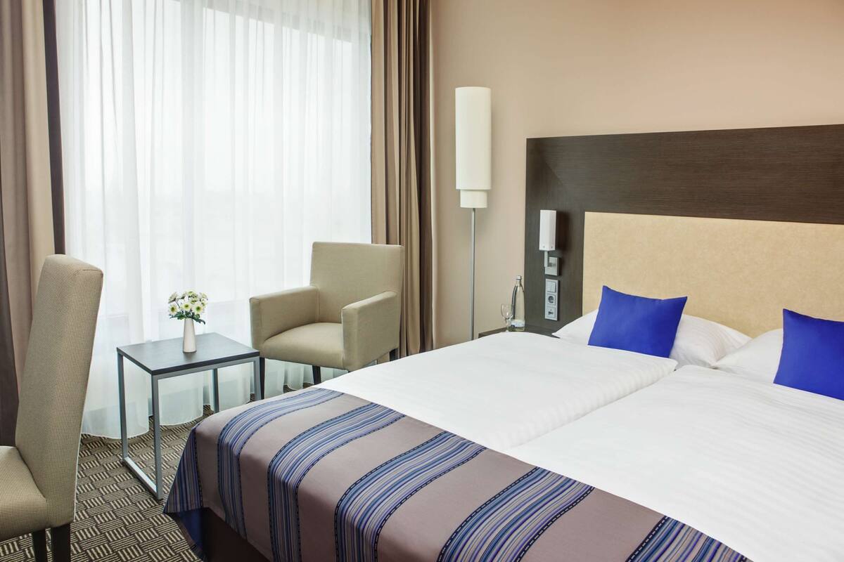 Une chambre d’hôtel avec un grand lit, deux chaises, une petite table avec un vase et une lampe.