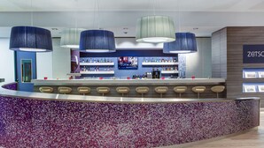 Un bar moderno con barra curva, diversas opciones de asientos y una variedad de botellas en estanterías.