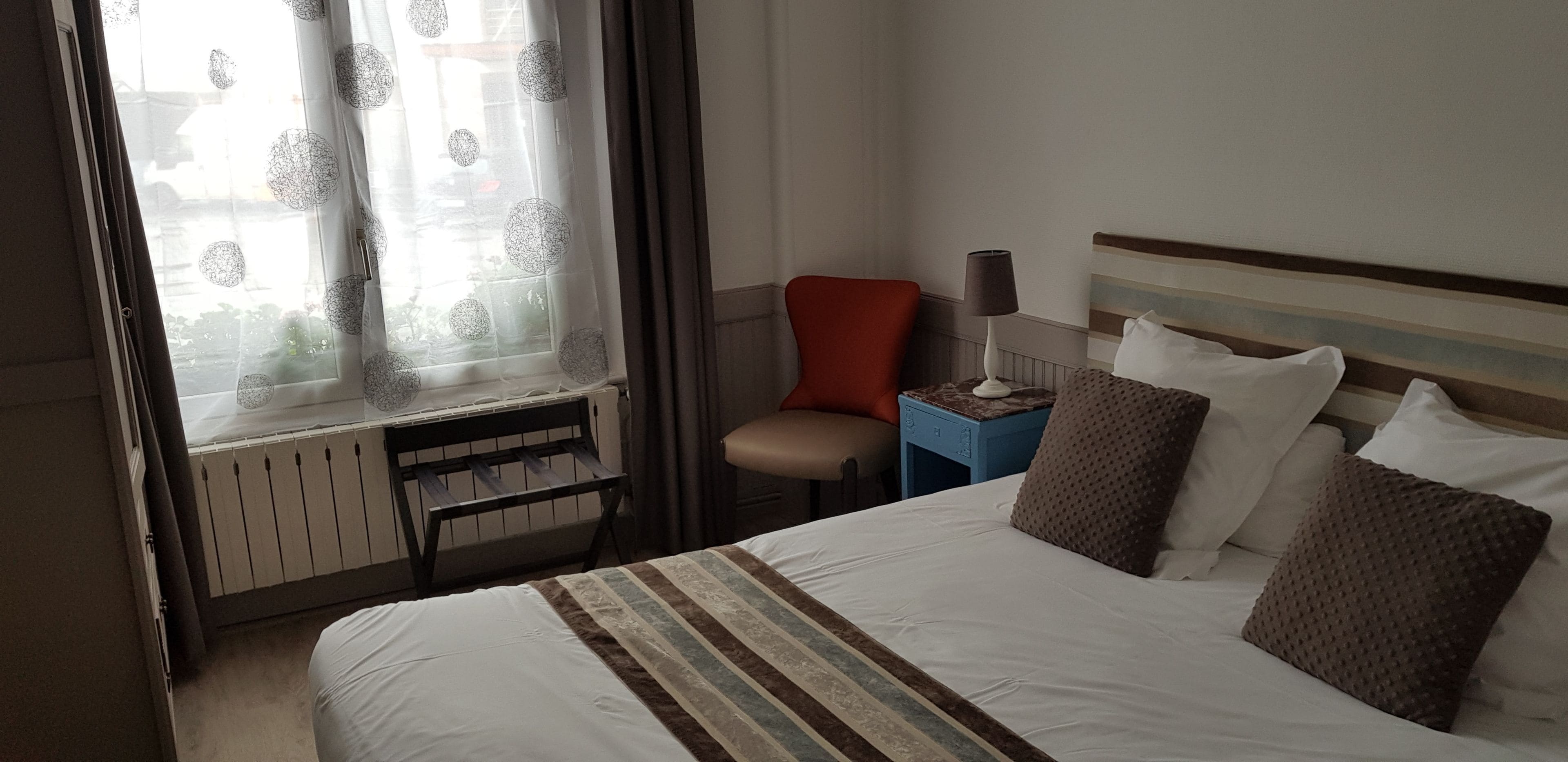 A hotel room with a bed, a chair, a nightstand, and a window with curtains.