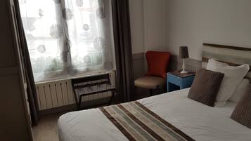A hotel room with a bed, a chair, a nightstand, and a window with curtains.