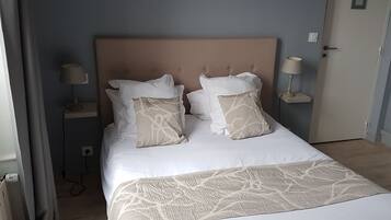 Un lit bien fait, recouvert d’une couvre-lit à motifs et agrémenté de deux coussins décoratifs, une table de chevet avec une lampe, et une porte avec un interrupteur.