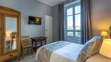 Una habitación de hotel con cama, armario de madera, televisión, una mesita y ventana con cortinas.
