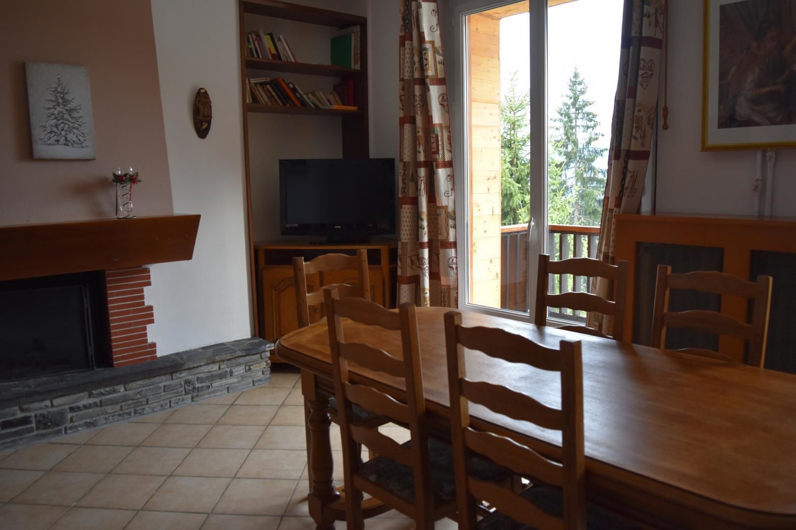 A dining area with a wooden table and chairs, a fireplace, a bookshelf, and a television.