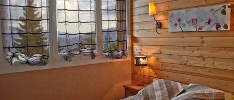 Un dormitorio con cama, mesita de noche, lámpara y ventana con cortinas.