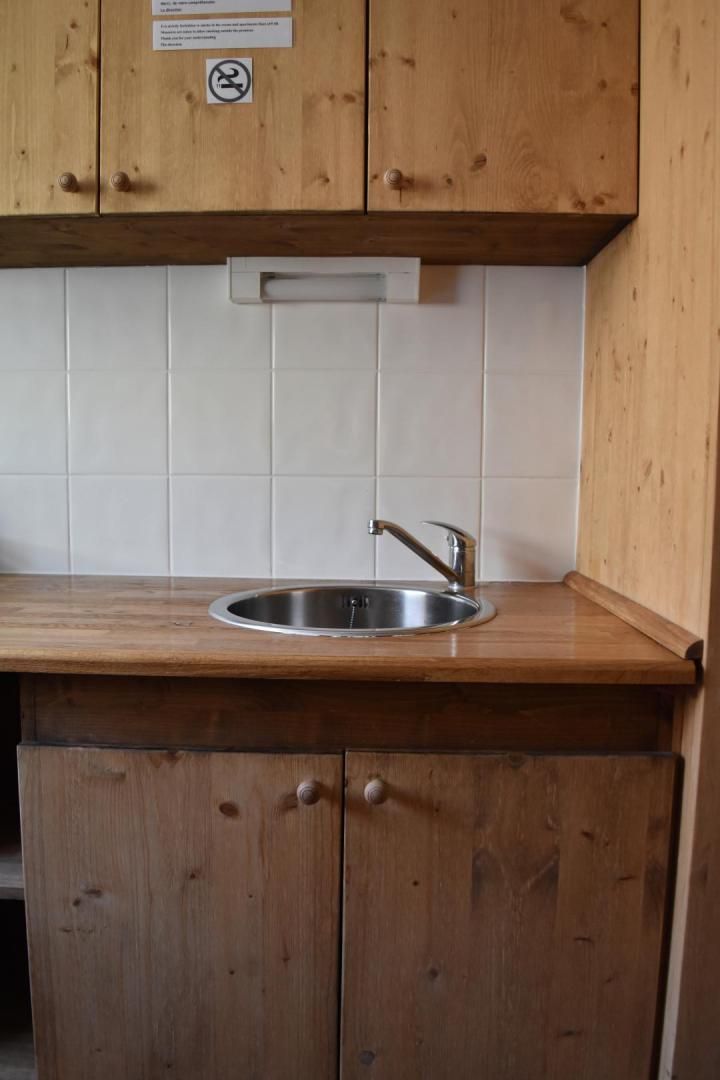 A kitchen with wooden cabinets, a stainless steel sink, and a white tiled backsplash.