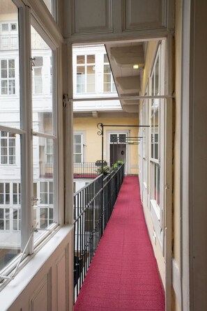 A corridor with a red carpet, white walls, and black railings. - Pertschy Palais Hotel (Vienna)
