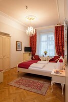A hotel room with a bed, a bedside table with a lamp, a TV, a wardrobe, and a large window with curtains.