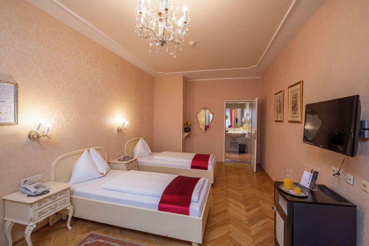 Quarto de hotel com duas camas, televisão, escrivaninha com telefone e minibar.