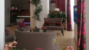 A spacious living area with a sofa, armchairs, and a dining table. There are potted plants and a chandelier.