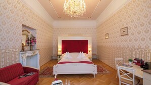 A luxurious bedroom with a large bed, a red sofa, a desk, and a chandelier.