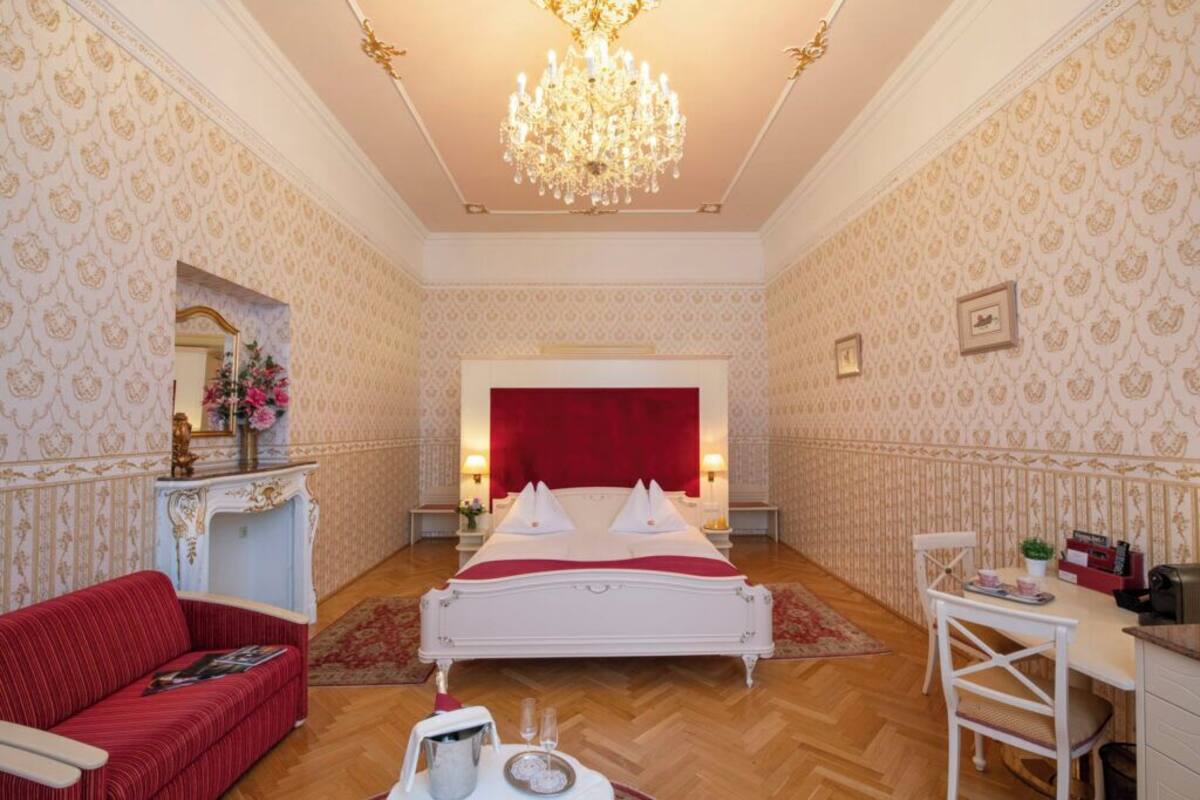 Um quarto luxuoso com uma cama grande, um sofá vermelho, uma escrivaninha e um candelabro.