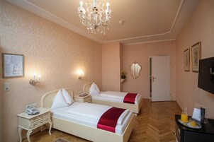 Een hotelkamer met twee bedden, een kroonluchter, een nachtkastje met telefoon, een spiegel en een deur.
