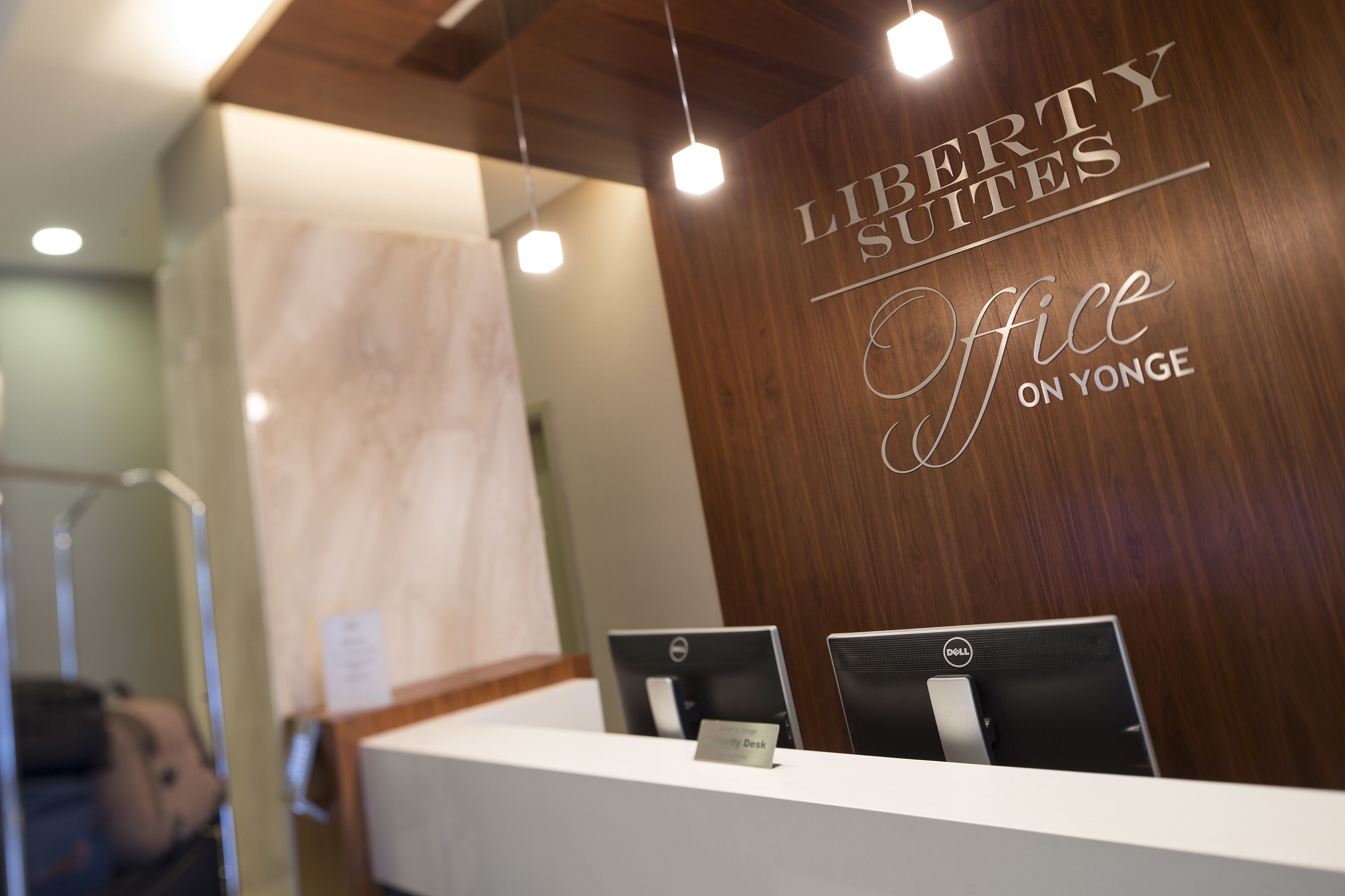 A reception desk with two Dell computers, a nameplate, and a wooden wall with the text "Liberty Suites Office on Yonge".