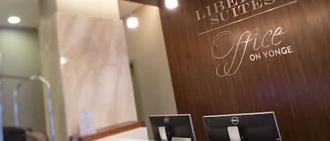 A reception desk with two Dell computers, a nameplate, and a wooden wall with the text "Liberty Suites Office on Yonge".