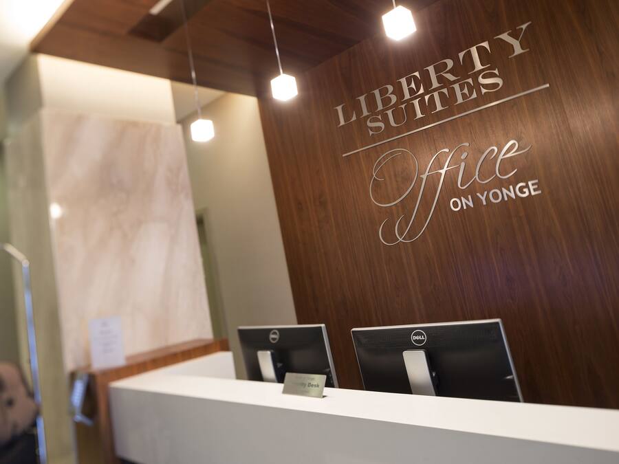 A reception desk with two Dell computers, a nameplate, and a wooden wall with the text "Liberty Suites Office on Yonge".