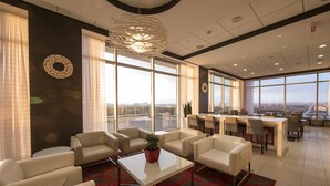 Un moderno vestíbulo de hotel con un área de estar, una recepción y grandes ventanales con vistas a la ciudad.