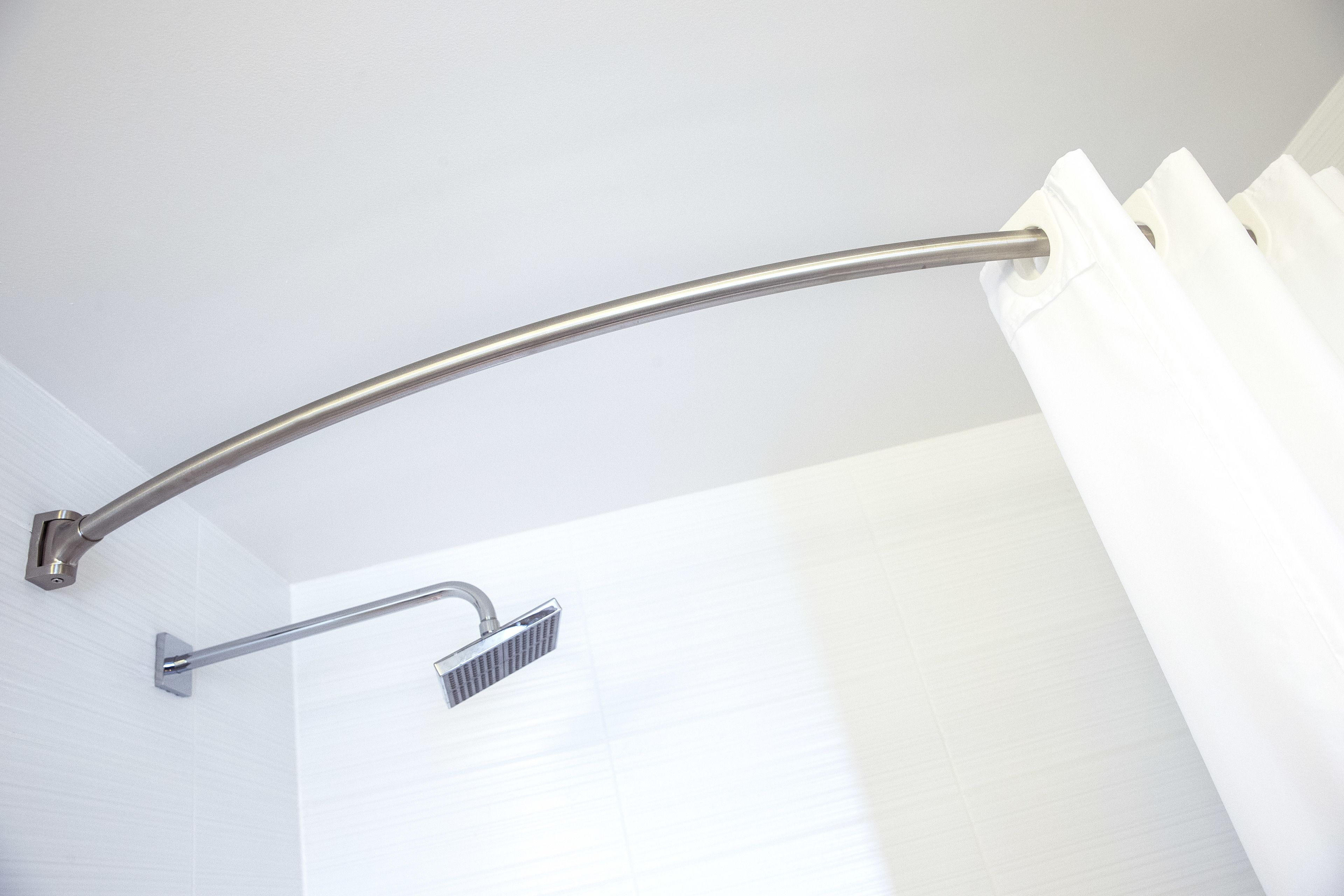 A shower area with a curved metal grab bar and a handheld showerhead.