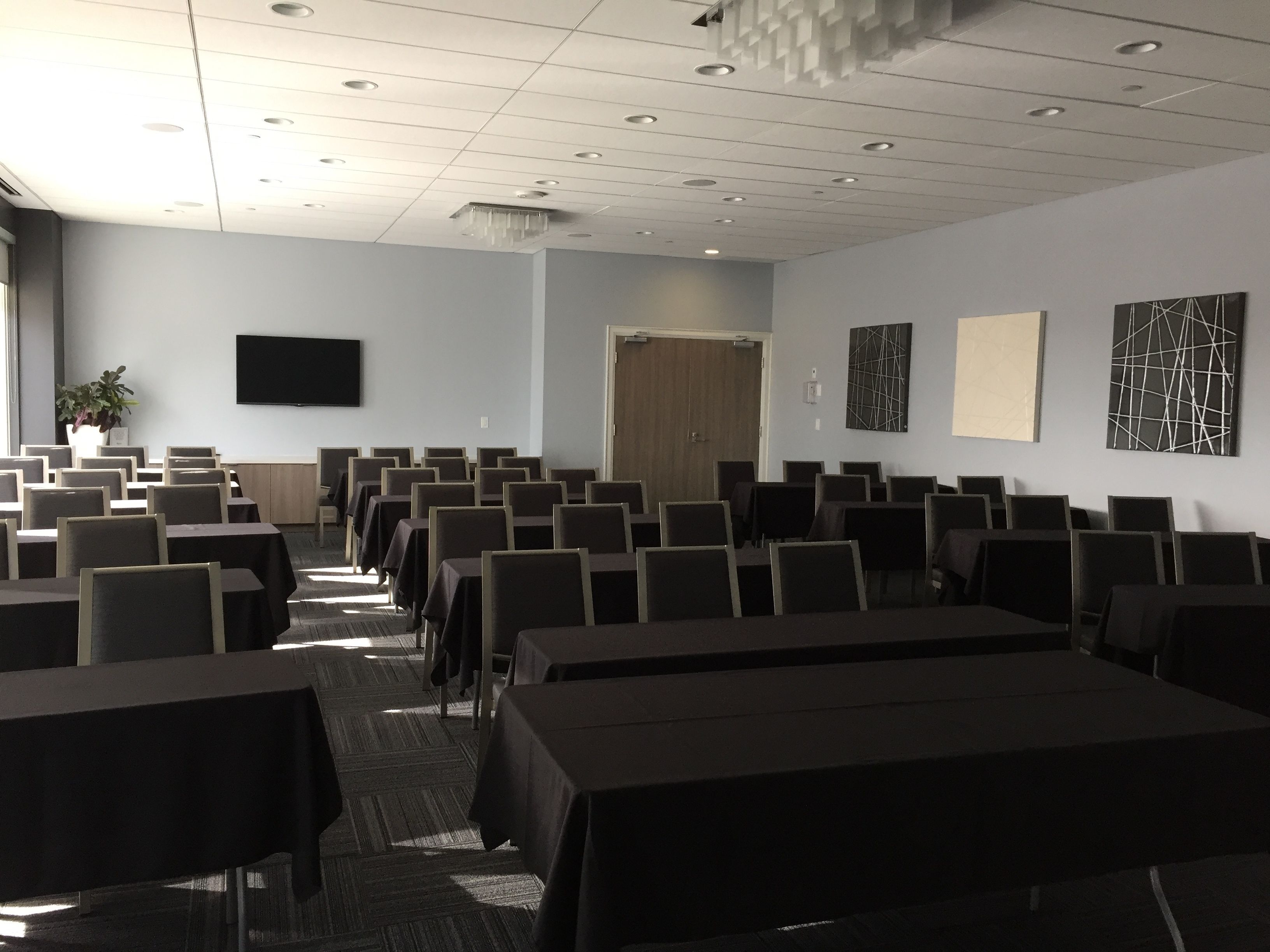 A conference room with rows of tables and chairs, a flat-screen TV on the wall, and abstract art pieces.