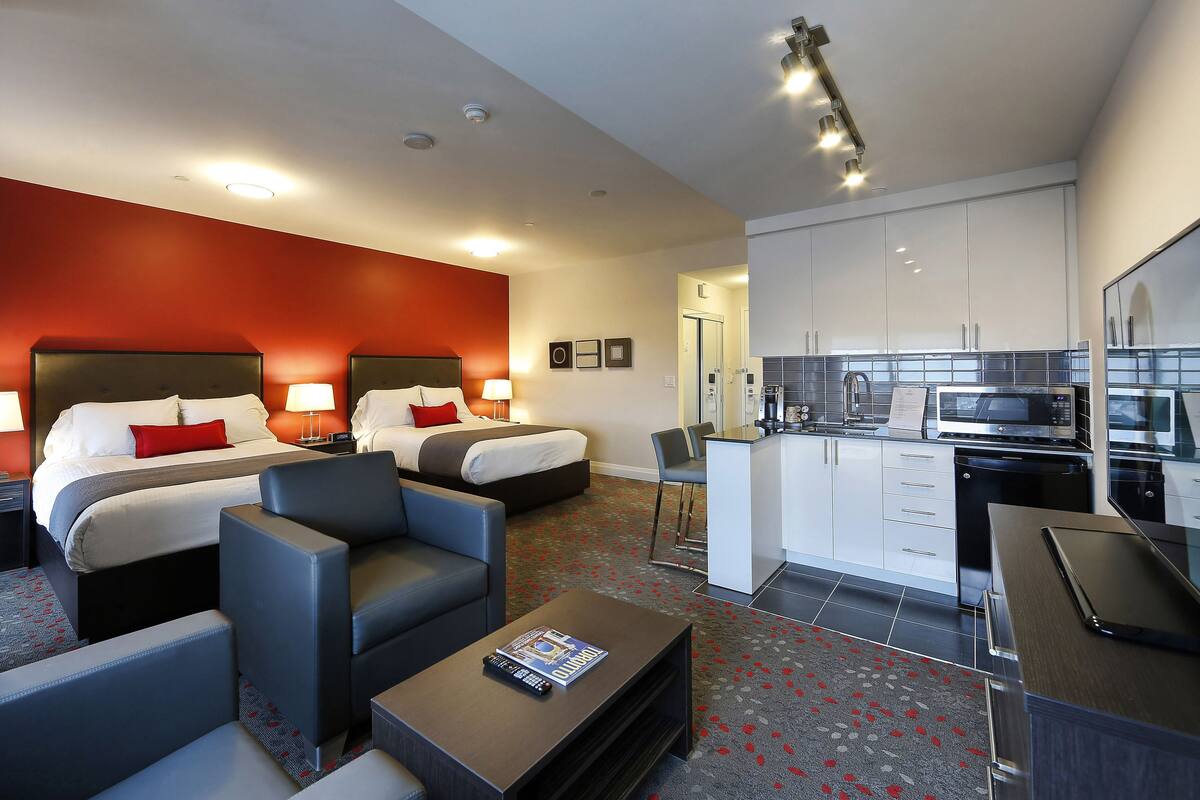 A hotel room with two beds, a sofa, a coffee table, and a kitchenette.