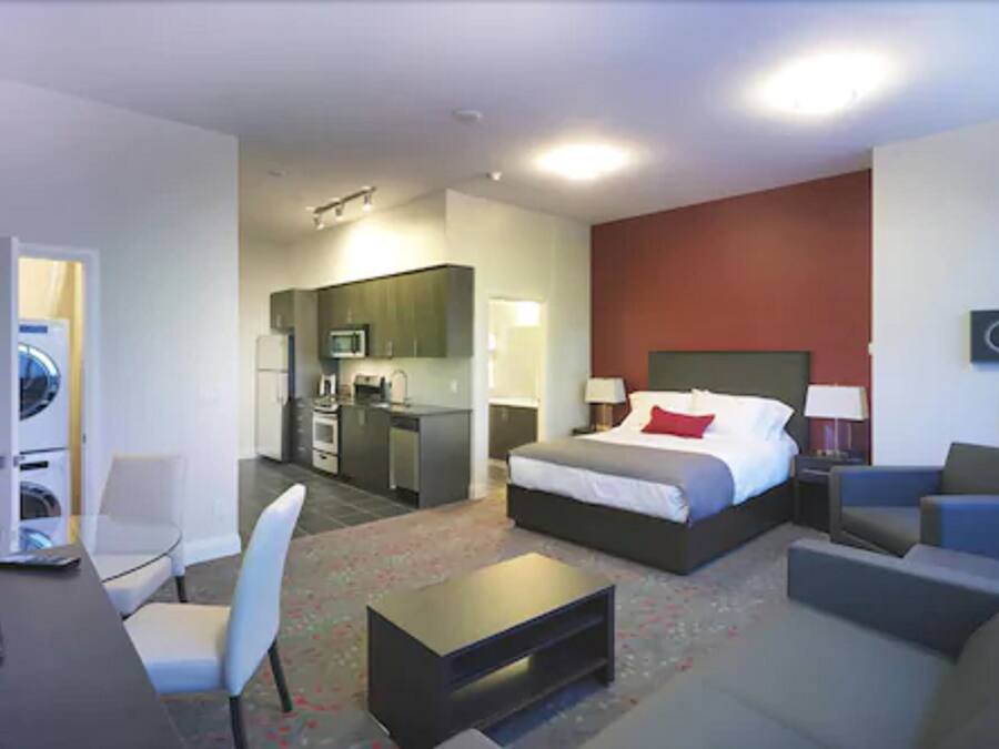 A hotel room with a bed, a desk, a chair, a sofa, a coffee table, a microwave, a refrigerator, and a washing machine.