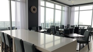 Una sala de conferencias moderna con una gran mesa y sillas, ventanas amplias con cortinas y vistas a la ciudad.