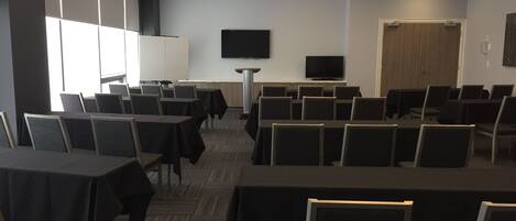A conference room with rows of tables and chairs, a television on the wall, and a door in the background.