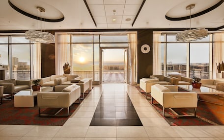 A spacious lobby with a view of the sunset through large windows, modern furniture, and a central pathway.