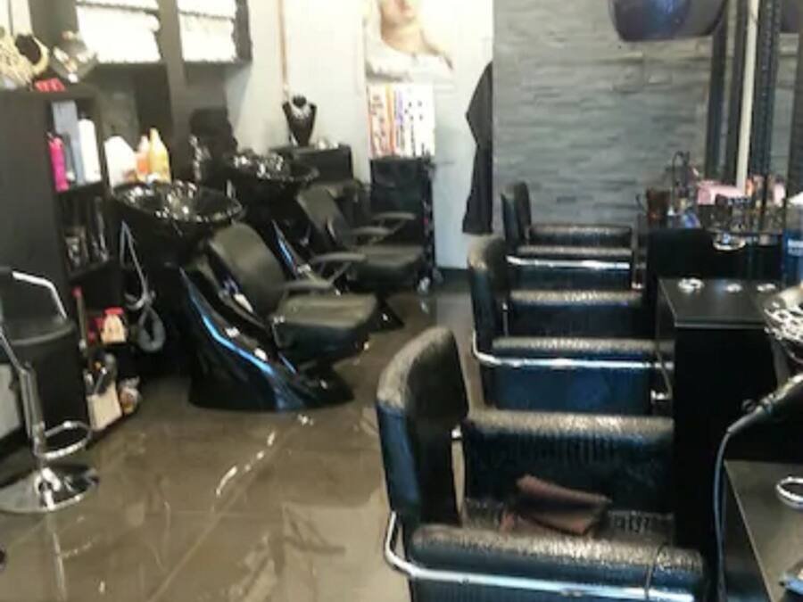 A salon with multiple black salon chairs, a mirror, and various hairdressing tools on shelves.