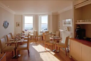 A dining area with multiple tables and chairs, large windows, and a view of the sea.