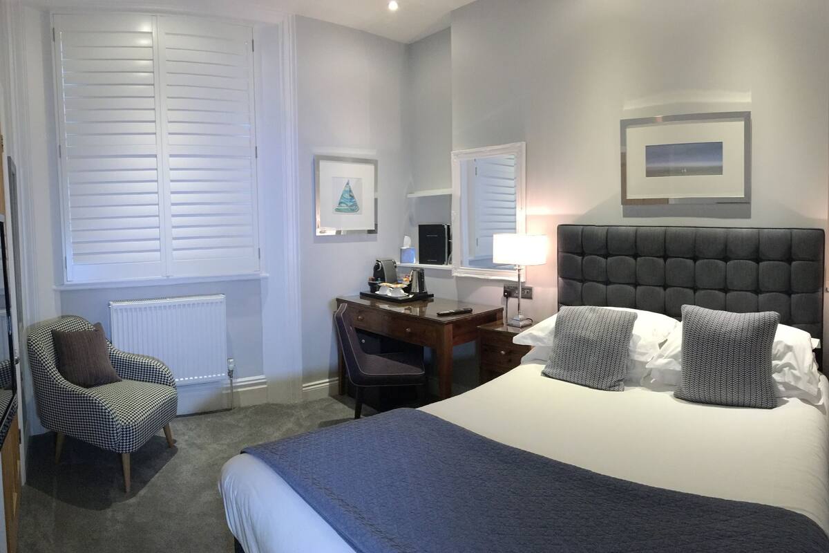 A hotel room with a large bed, a desk, a chair, and a dresser.