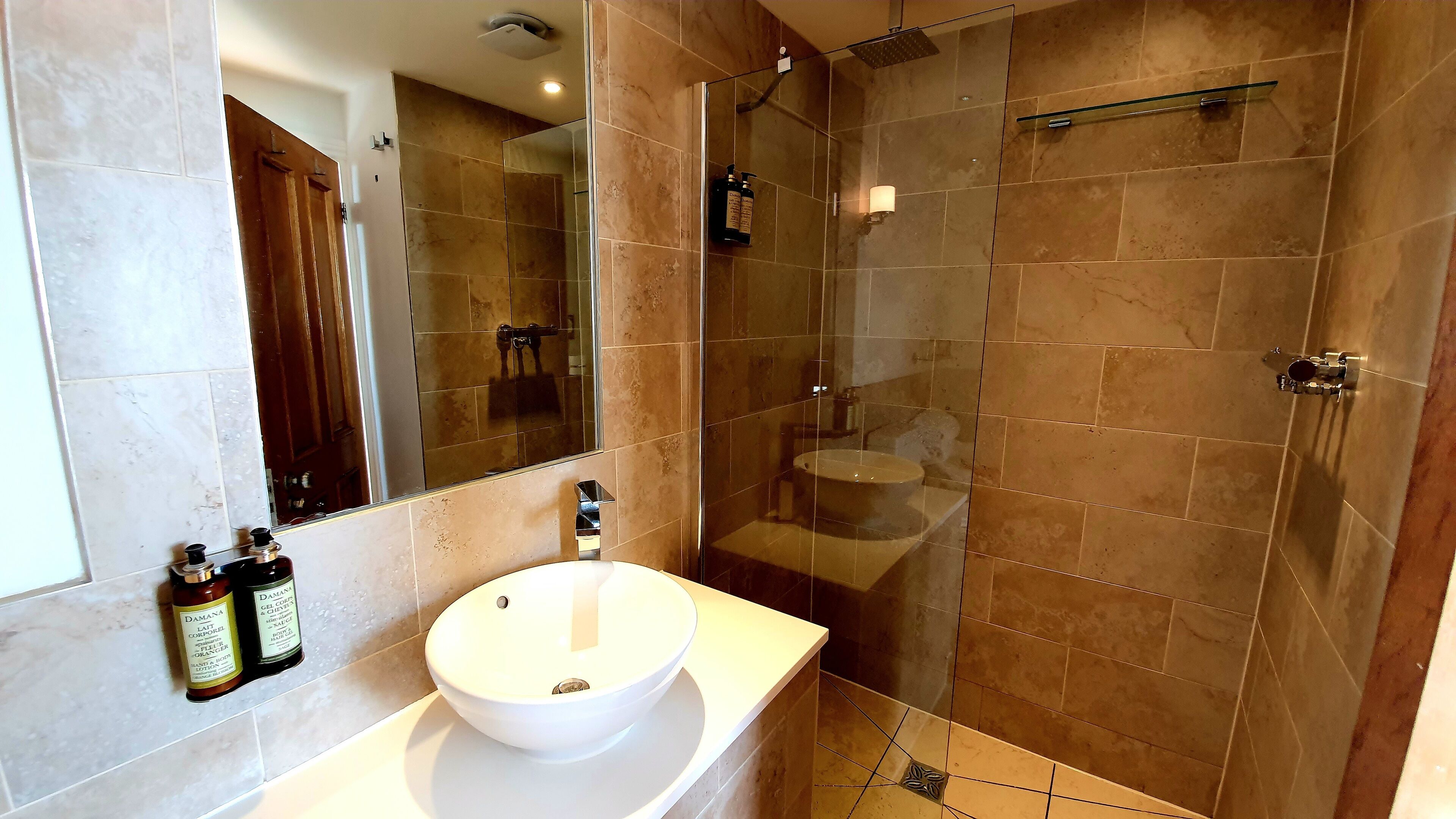 A bathroom with a white sink, a glass-enclosed shower, and two bottles of lotion on the counter.