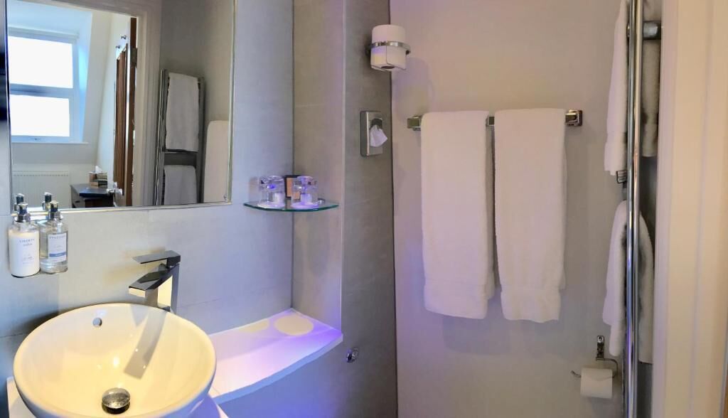 A bathroom with a round sink, a mirror, a glass shelf with toiletries, a towel rack, and a shower area.