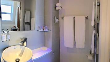 A bathroom with a round sink, a mirror, a glass shelf with toiletries, a towel rack, and a shower area.