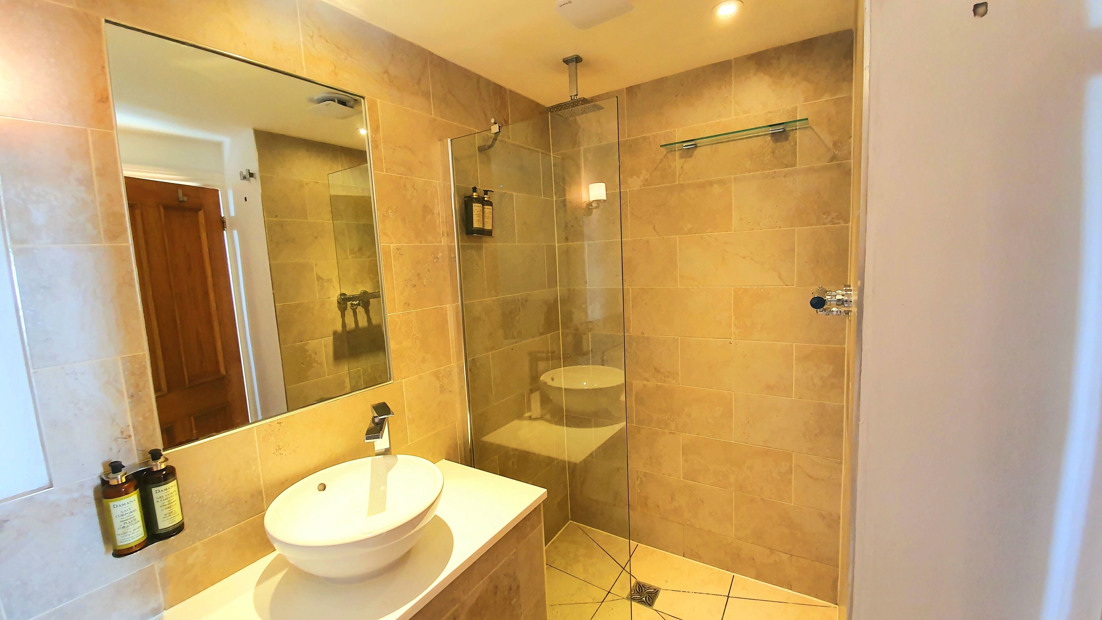 A modern bathroom with a large mirror, a white sink, and a glass-enclosed shower area.